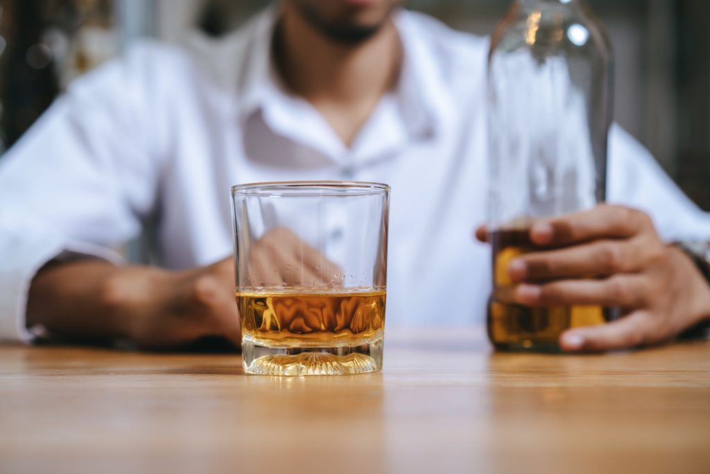 Man holding a glass of whiskey, reflecting addiction and dependency