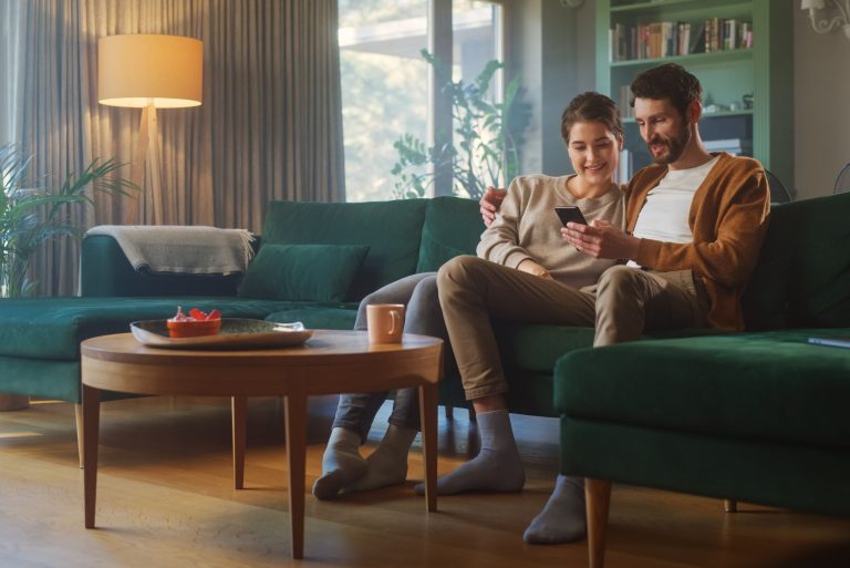 A couple sitting on a living room couch, engrossed in their phone, enjoying each other's company