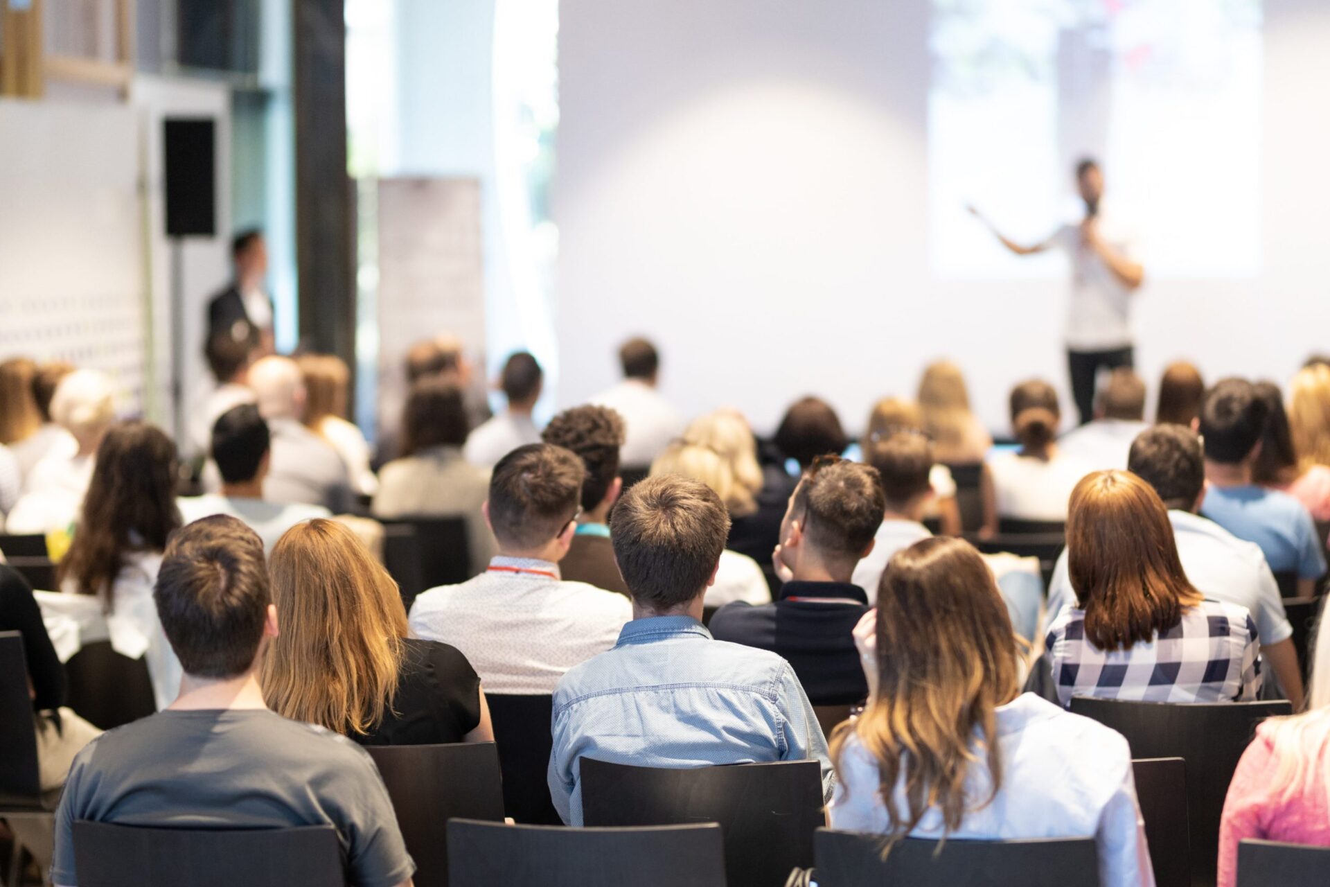 Audience seated in front of a speaker, with a man giving a presentation