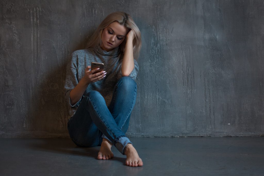 A woman sitting down, engrossed in her phone, seemingly facing some issues or challenges