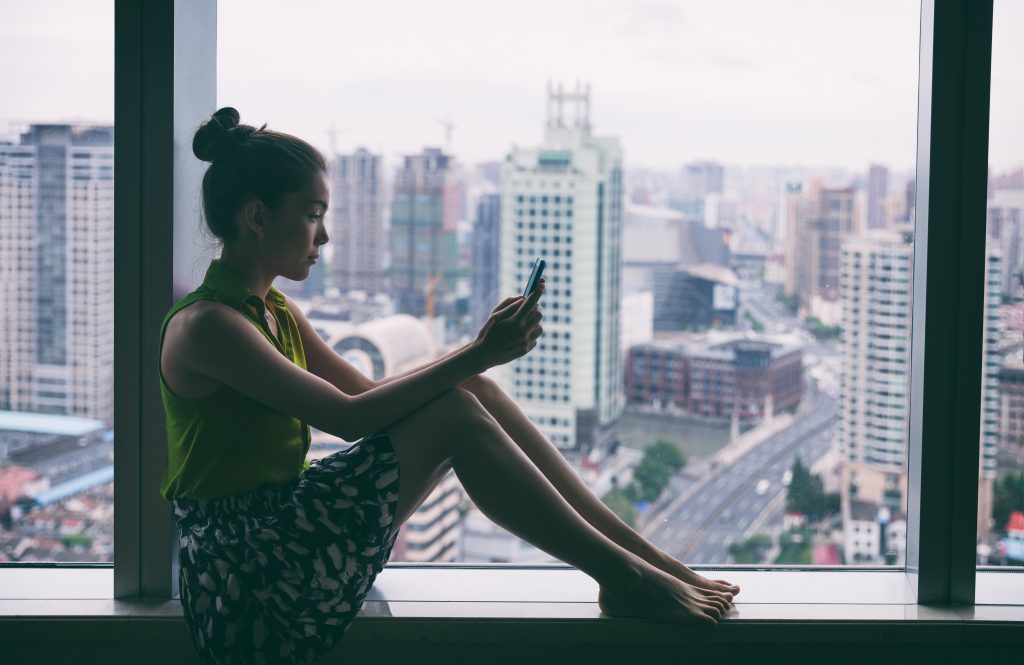 A woman sitting on a window sill, engrossed in her phone