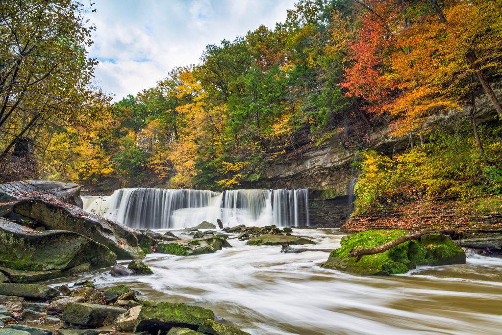 A picturesque fall waterfall surrounded by vibrant trees, with water flowing gracefully down the rocks