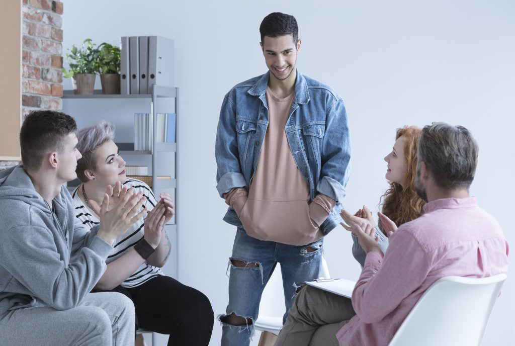 Five people talking and clapping for the person standing