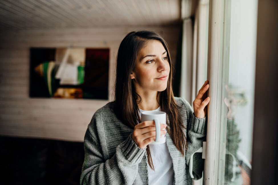 Woman holding a cup of coffee, gazing out the window