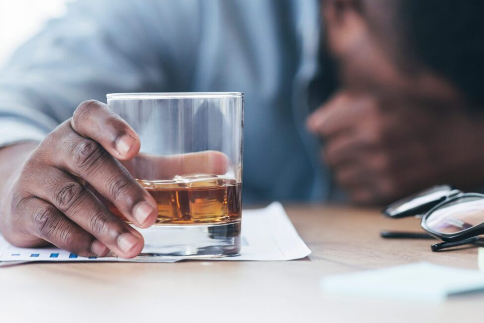 Man holding a glass of whiskey, reflecting addiction and dependency