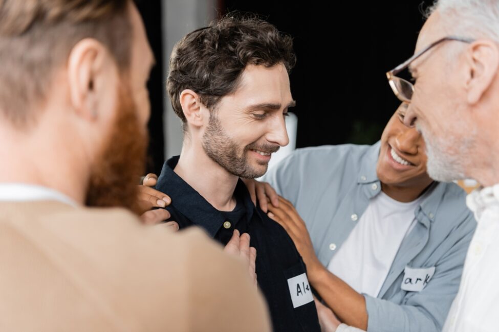 A group of men engaged in conversation, wearing smiles on their faces. One man is encouraged, holding his shoulder with a smile