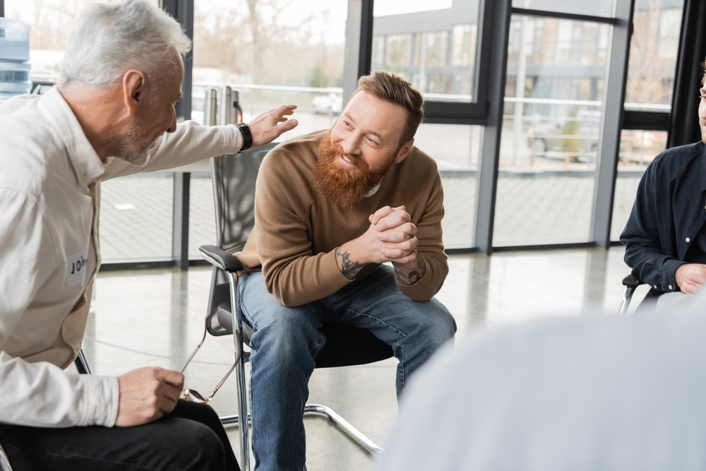 Man with a beard happily touching the shoulder of an older man